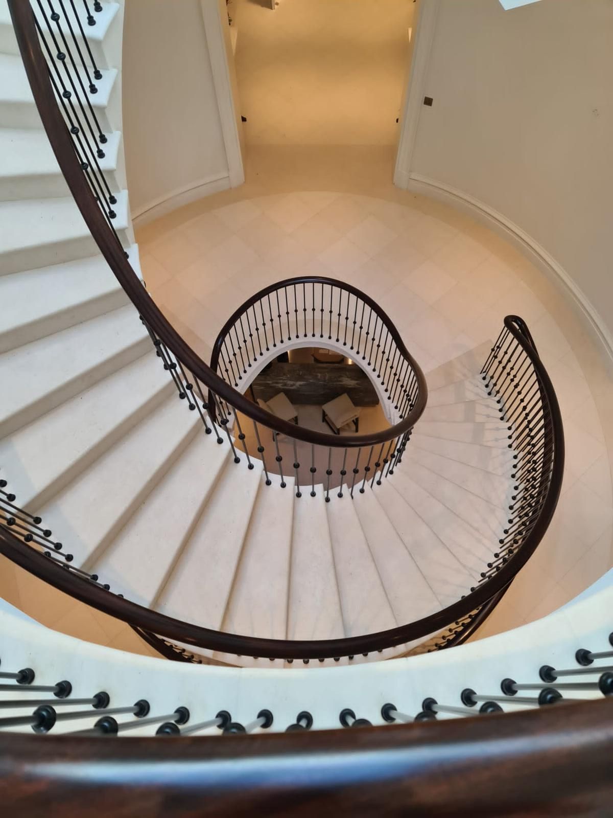 Looking down a sweeping cantilevered staircase with a dark handrail and white stone treads